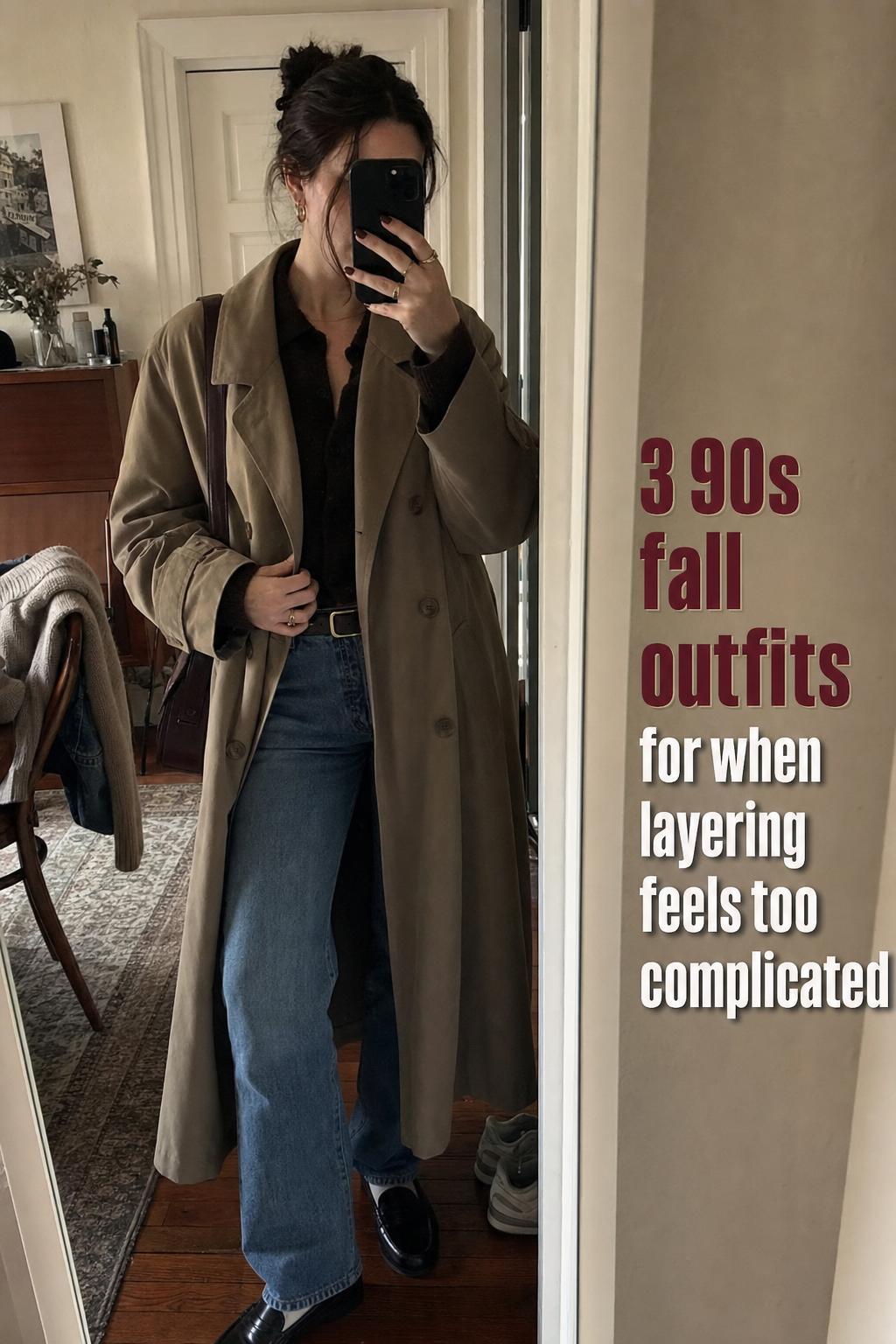 Mirror selfie of casual 90s fall outfits look with trench coat, straight-leg jeans, knit top and loafers in a lived-in apartment