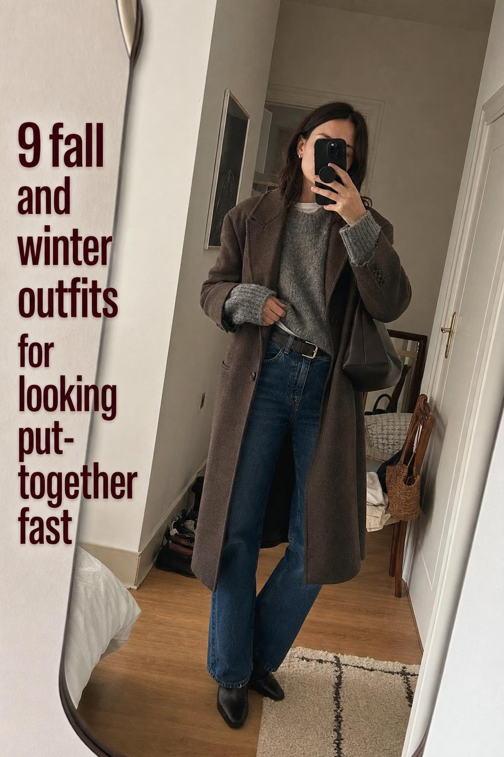Mirror selfie of a woman layering knit sweater and wool coat in an apartment hallway, showcasing fall and winter outfits
