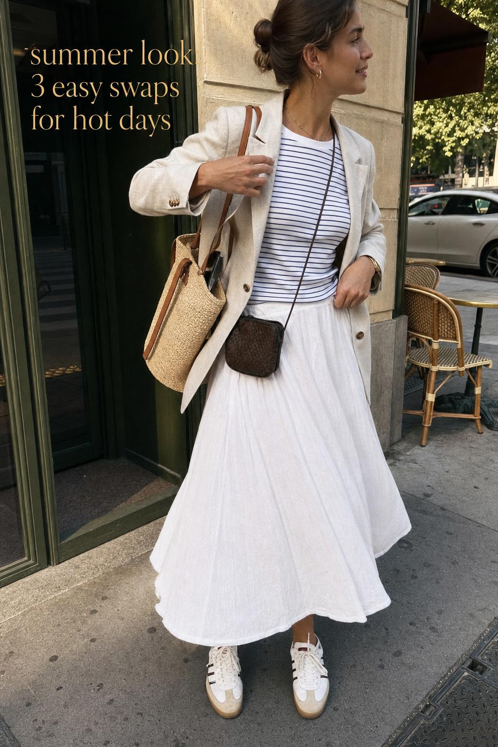 Summer look street style: woman adjusting linen blazer on city sidewalk by cafe in a breathable tee and midi skirt