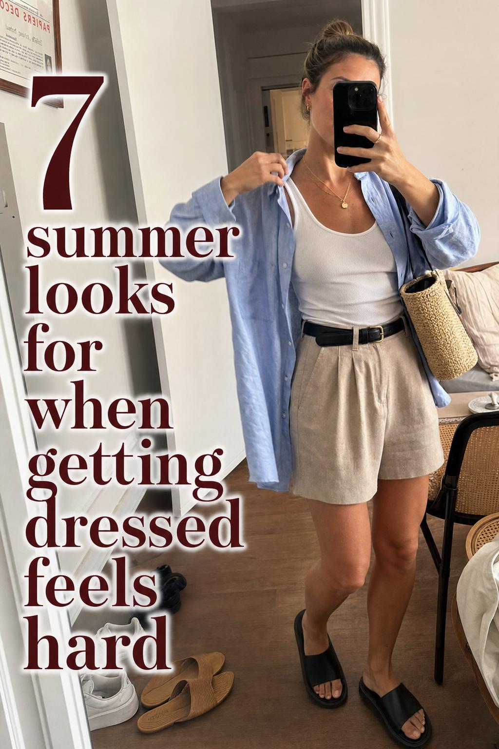 Summer looks mirror selfie in a messy apartment hallway, linen shirt and shorts outfit with sandals and tote bag