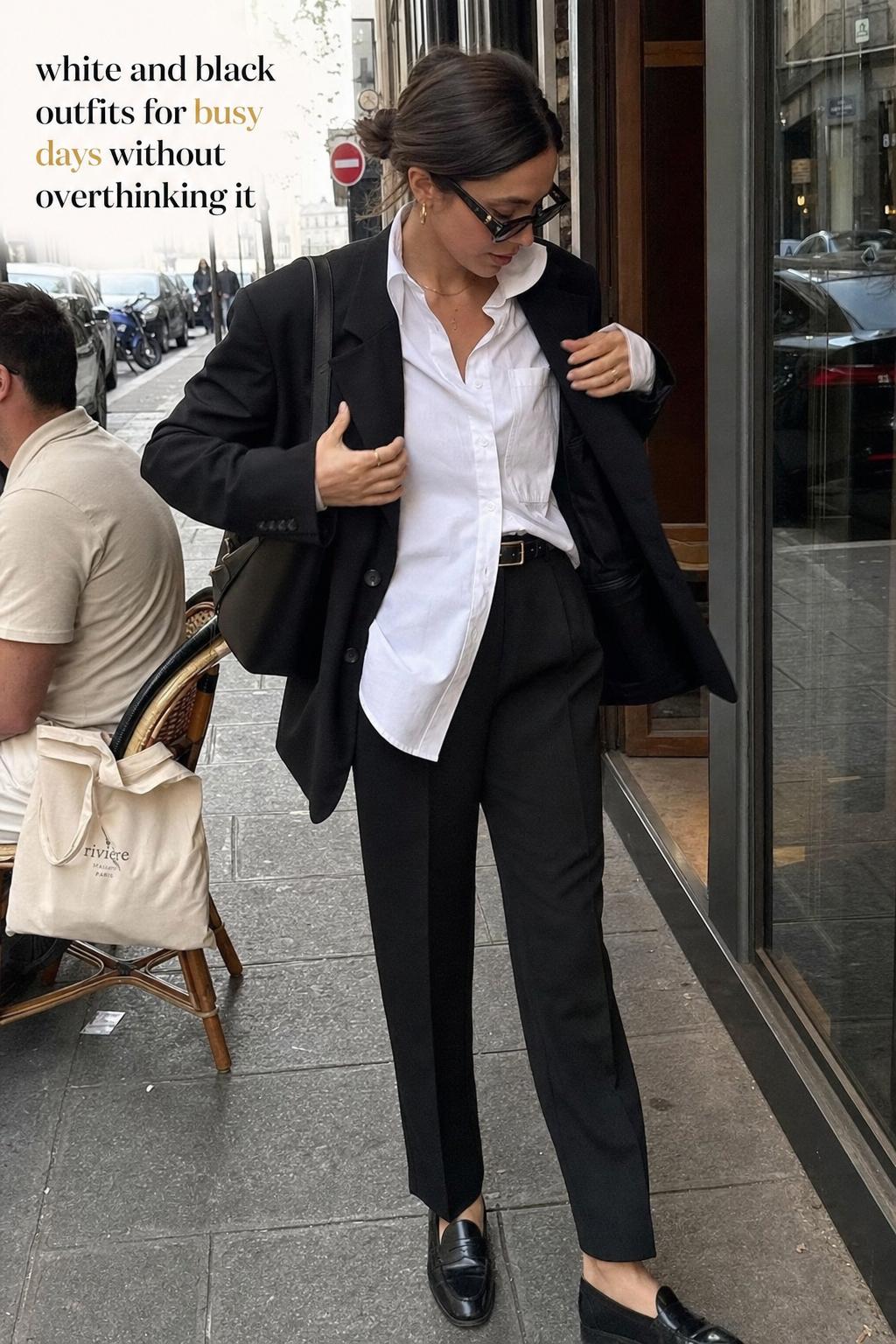 Candid city street photo of a woman adjusting a blazer in white and black outfits outside a cafe in natural daylight