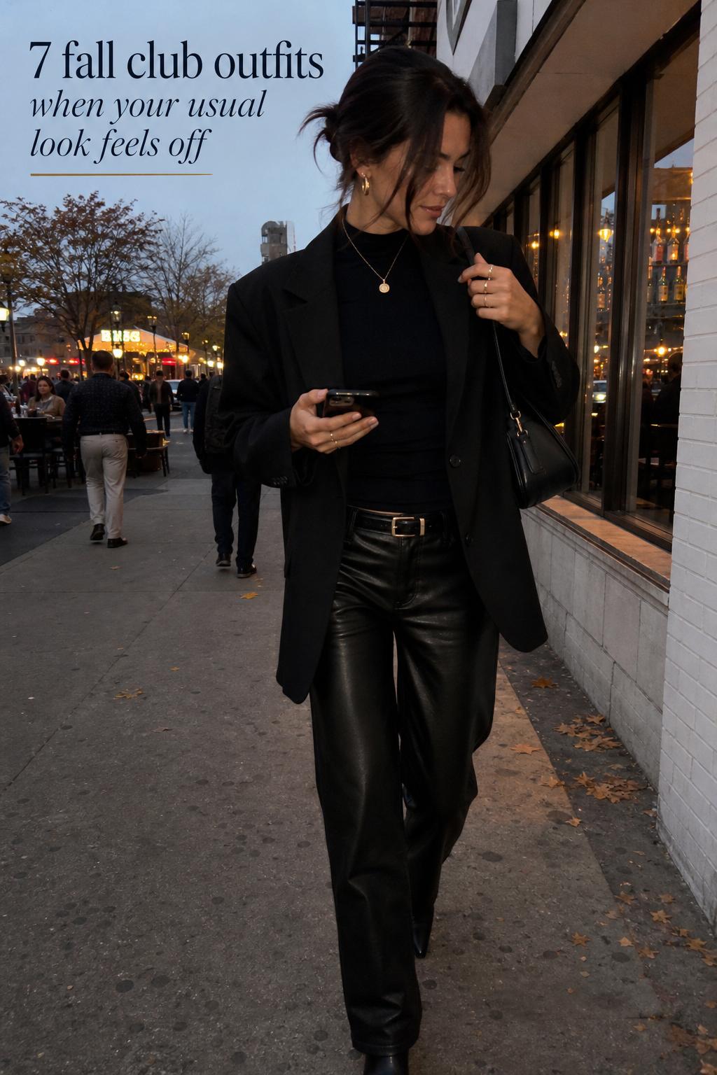 Fall club outfits street style: woman in black blazer and faux leather pants walking past a bar at dusk