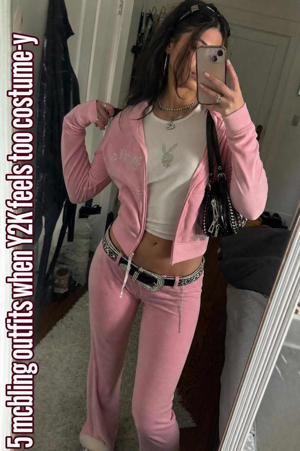 Mirror selfie of a young woman in pink velour mcbling outfits with rhinestone belt and bag in a lived-in bedroom