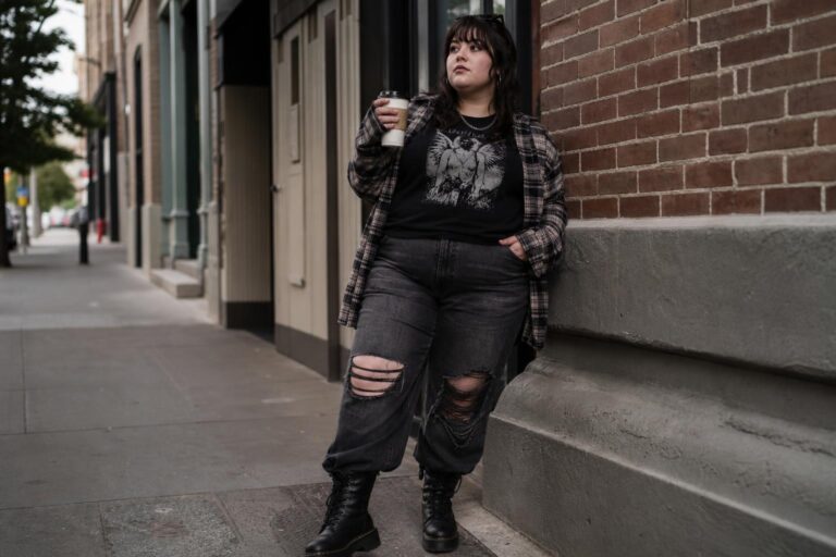 Plus size grunge outfits with band tee, open plaid flannel, ripped jeans and combat boots on a city street