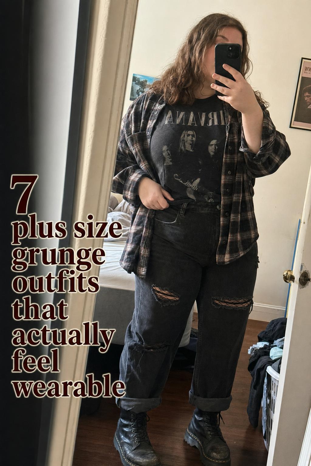 Mirror selfie of a plus-size woman in plaid flannel, band tee and ripped jeans showcasing plus size grunge outfits in an apartment hallway.