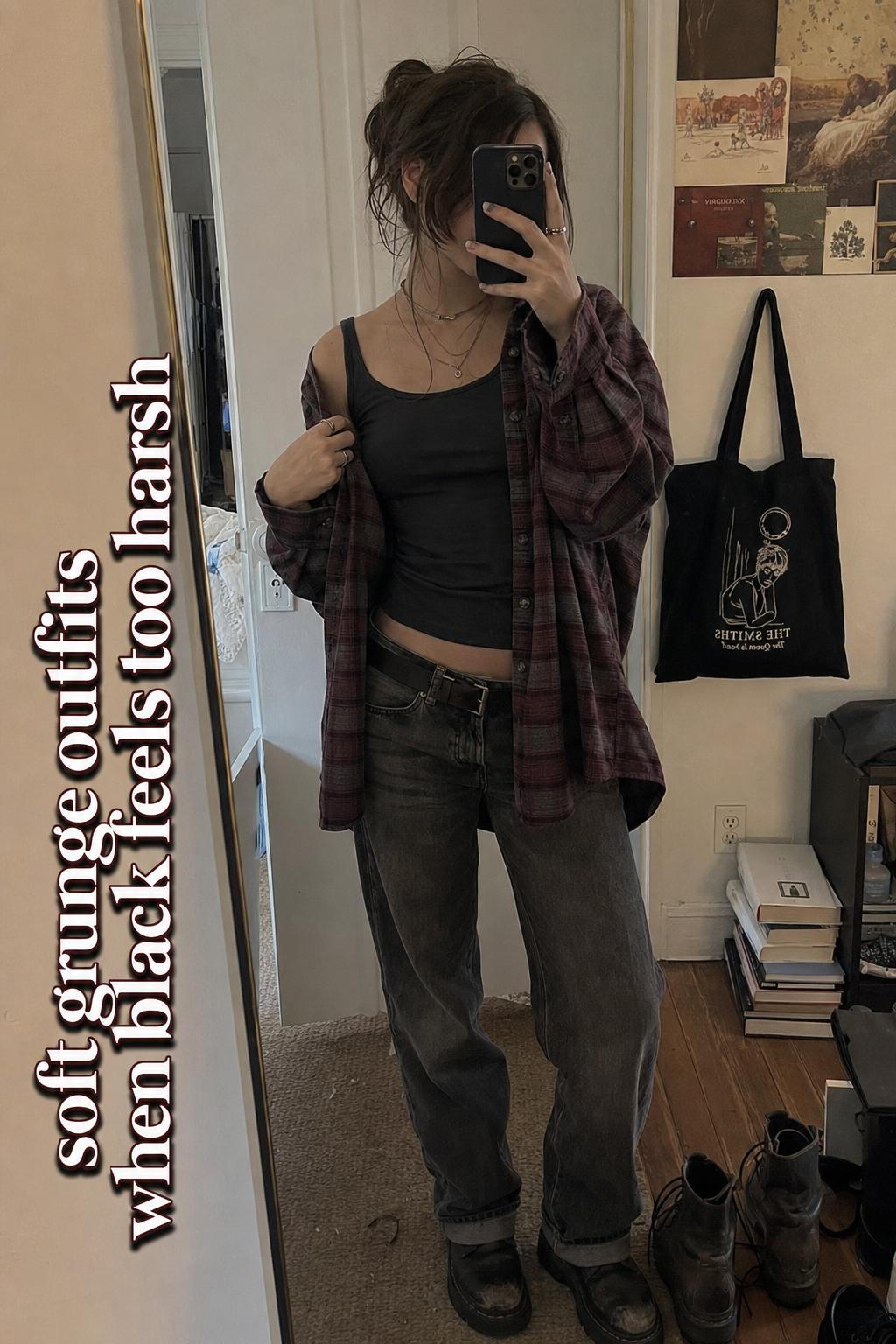 Soft grunge outfits mirror selfie of a young woman in burgundy flannel, washed black tee, faded denim and worn boots at home
