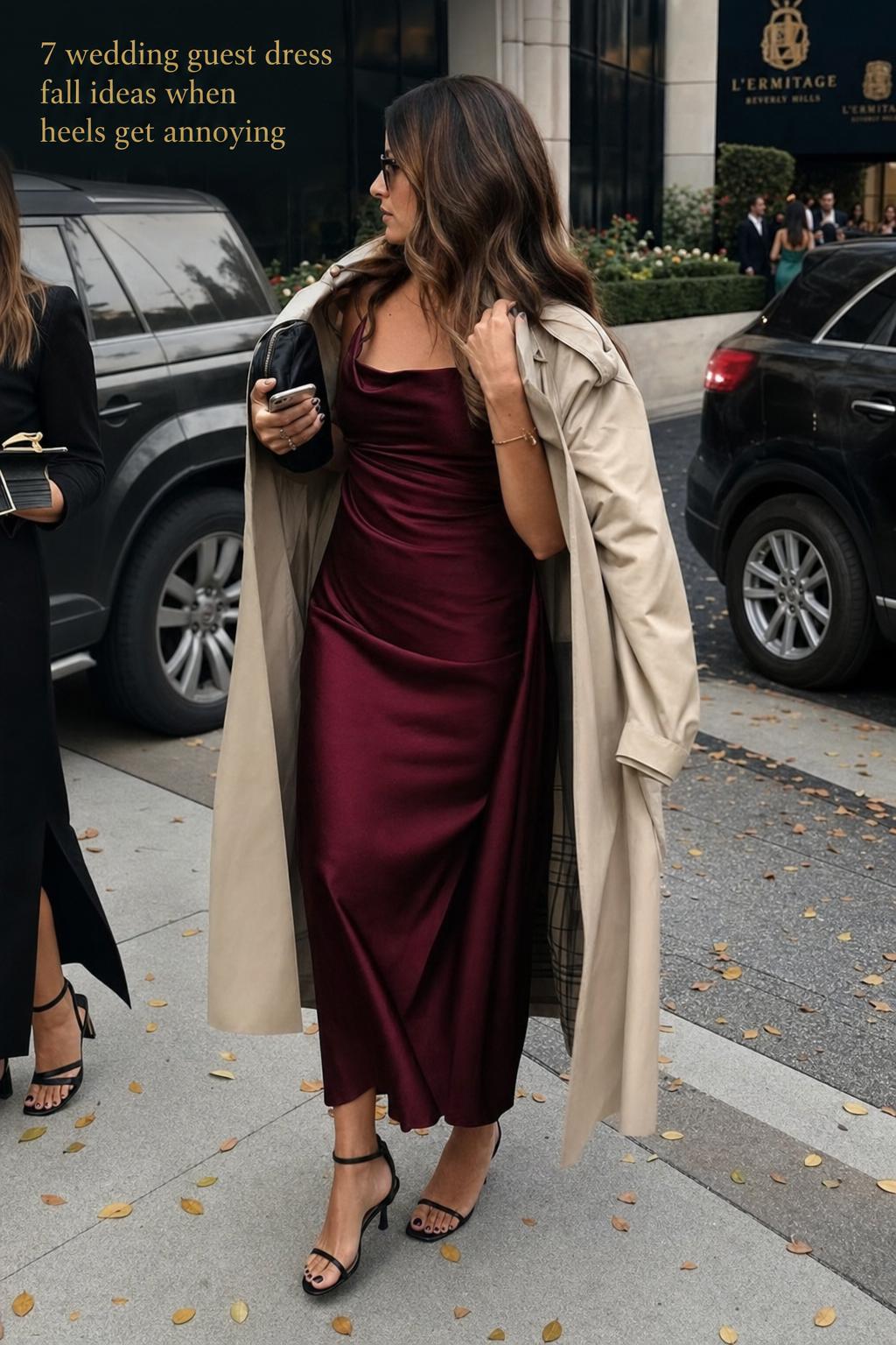 Woman adjusting trench coat over satin midi outfit on city sidewalk, wedding guest dress fall style in real-life candid light